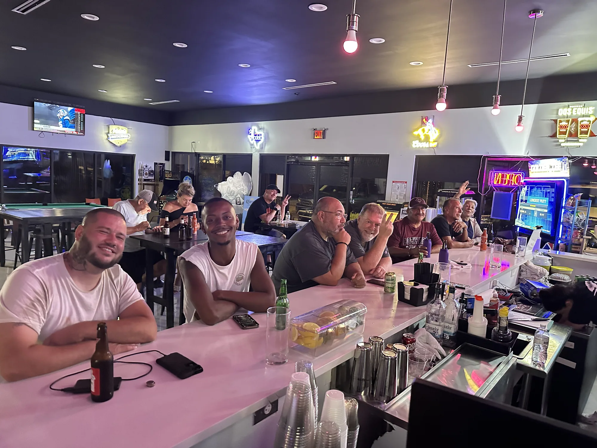 Friends lined up along The 183's white bar under a row of TVs and pendant lights